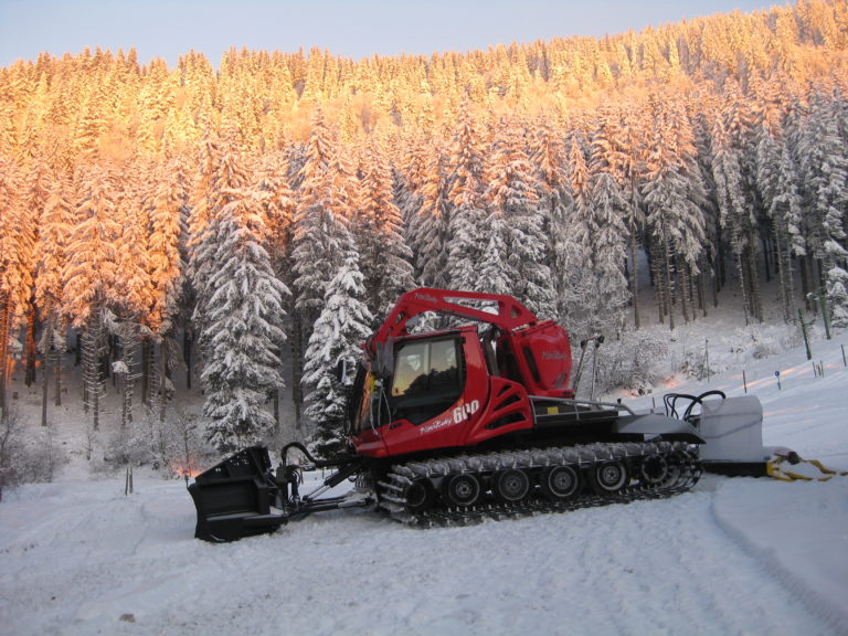 Chasse neige n'actions sur les pistes avec un lever de soleil sur la forêts du domaine alpin du ski club du Barioz